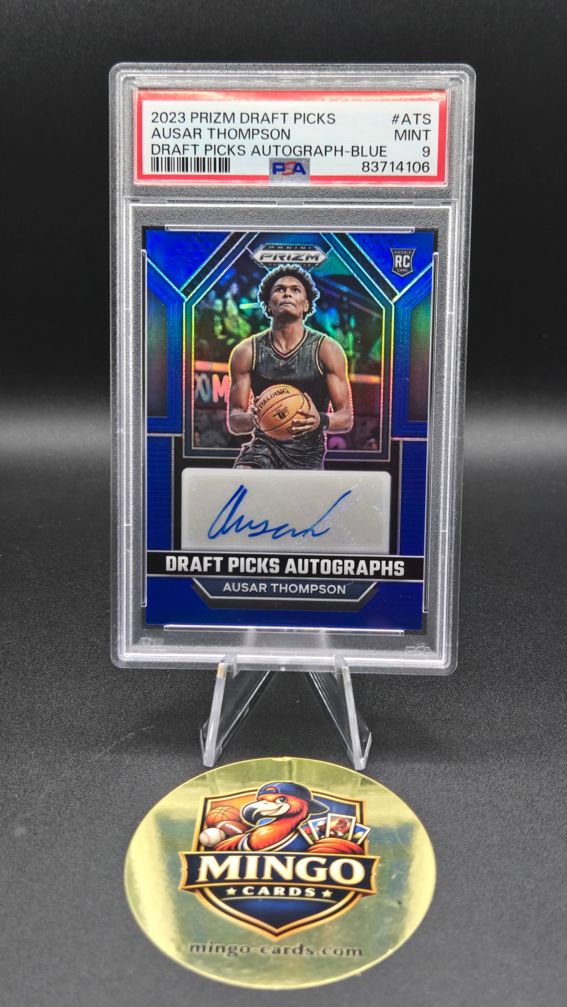 A 2023 Prizm Draft Picks card in a clear PSA holder graded PSA 9 next to a gold Mingo Cards collectible coin on a dark background.