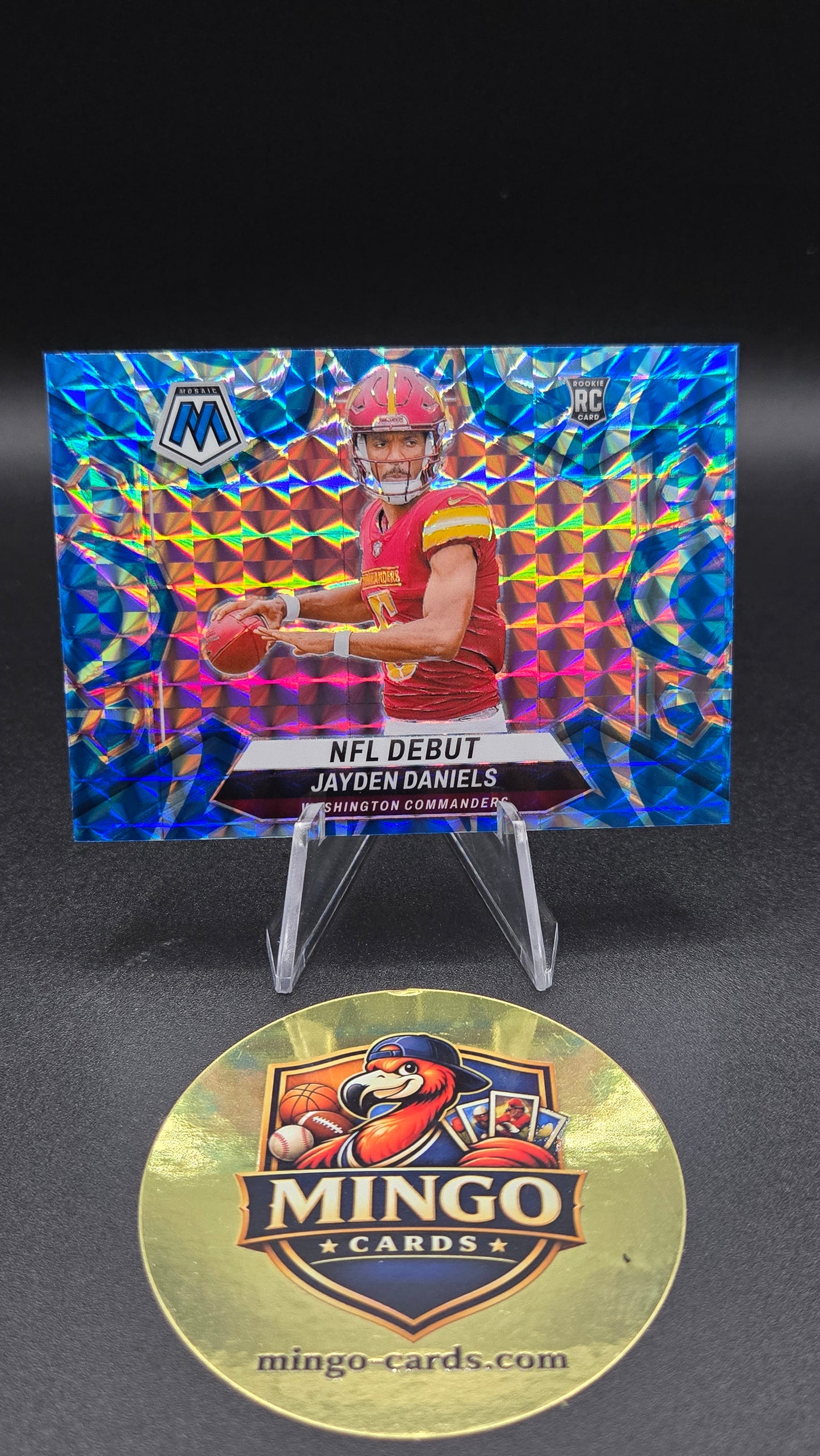 A collectible football trading card featuring Jayden Daniels a holographic blue and pink background, displayed next to a round gold Mingo Cards logo medallion on a black surface.