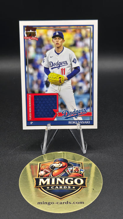 A baseball trading card of Roki Sasaki on a clear display stand next to a round gold Mingo Cards brand medallion on a black background.